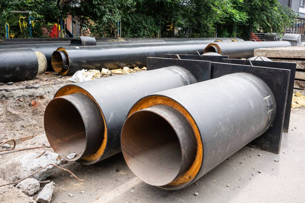 Closeup view of two new insulated water pipes on city road in summer day.